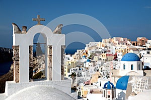 View of sea surface through traditional Greek white church arch with cross and bells in Oia village of Cyclades Island, Santorini,