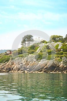 View from the sea to the greeny cliffs with exotic trees, moss and blue sky.