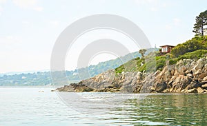 View from the sea to the greeny cliffs with exotic trees, moss and blue sky.