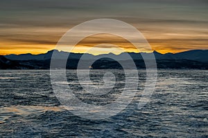 View from the sea to the setting sun behind the mountains. Dark time of day.