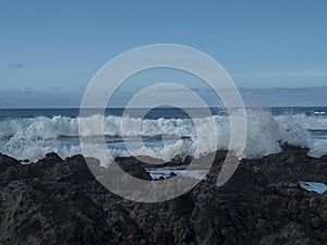 View of sea vawes crushing against black and brown volcanic lava rocks. Water splash at Tenerife atlantic ocean rugged