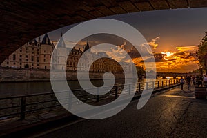 View of Seine river with Conciergerie palace, bridge over the Seine river and Parisians walking on the embankment at sunset