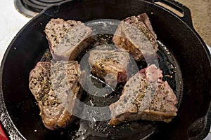 View of several juicy lamb chops sizzling in a hot cast iron skillet on a white stove top