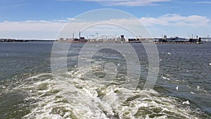 View of the shore and ocean from the stern of the ship.View of the waves following the ship in sunny weather.