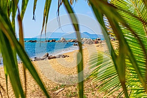 View of the shore of the South China Sea with a sandy beach, large rocks and green palm trees. Sanya, China.