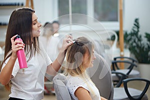 View from side of hairdresser fixing bouffant with hairspray in beauty salon