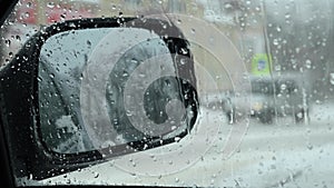 View in the side mirror of a car through transparent glass with drops from rain or snow against the background of a