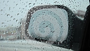 View in the side mirror of a car through transparent glass with drops from rain or snow against the background of a