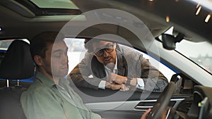 View through the side window of the car to stylish sales manager wearing business suit talking to male client sitting in