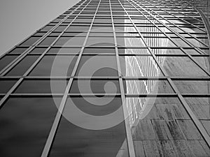 A view from the sidewalk in front of a glass sky scraper shows a reflection of the Grace building.