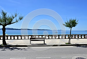 View of Silgar Beach from promenade with stone handrail and wooden bench. Rias Baixas, Pontevedra Province. Sanxenxo, Spain.