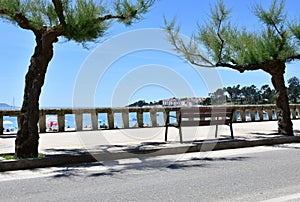 View of Silgar Beach from promenade with stone handrail and wooden bench. Rias Baixas, Pontevedra Province. Sanxenxo, Spain.