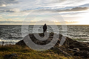 View of a silhouetted man standing the the rocky coastline on San Juan Island at sunset, with thin white clouds in the background