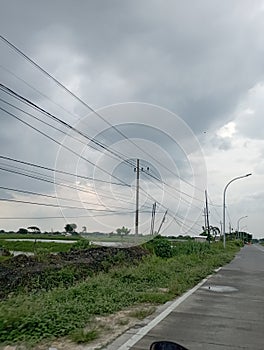 view of the sky, grass, streets, clouds and electricity poles in the village