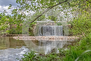 View of a small cascade on river, with trees, rocks and vegetation on the banks