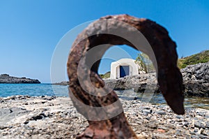 View of a small chapel by the sea through a rusty hook