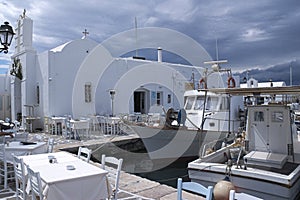 View of a small harbor with fishing boats and a taverna by a church at Naoussa, Paros, Greece.