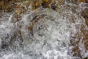 View of small waterfall on river with detail of water foam, rocks and river vegetation