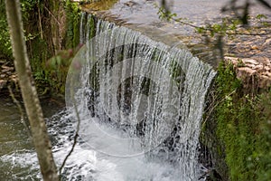 View of small waterfall on river with detail of water foam, rocks and river vegetation