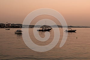 View of small, wooden fishing boats, Aegean sea and landscape at sunset captured in Ayvalik area of Turkey in summer.