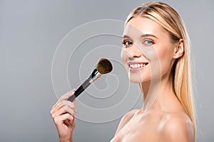 View of smiling naked woman with cosmetic brush isolated on grey