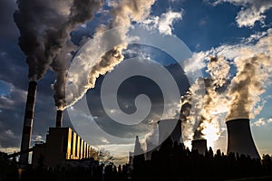 A view of the smoking chimneys of a coal-fired power plant against the backdrop of a dramatic sky with clouds.