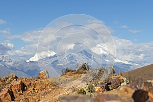 View of snow-capped mountains, mountains, meadow, some vegetation, rocks, sky and clouds in the afternoon, in Chicarhuapunta