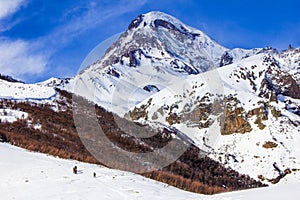 View of the snow-covered Kazbek, a group of skiers rises to the top