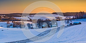 View of snow covered rolling hills and farm fields at sunset in