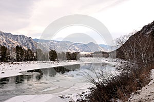A view of a snow-covered valley with a flowing melted river on a winter evening
