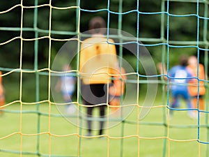 View through soccer gate net. The goalkeeper slowly backs up during the opponents attack. Abstract view