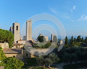 View of some of the towers of San Gimignano, Italy against blue sky, from the Parco della Rocca full of trees