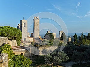 View of some of the towers of San Gimignano, Italy against blue sky, taken from the Parco della Rocca full of trees