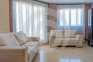 View of a spacious living room with lots of light beige sofas and two large windows