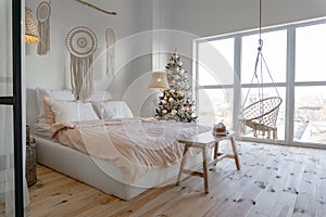 View on spacious white bedroom decorated with Christmas New year tree and tea set standing on a bench