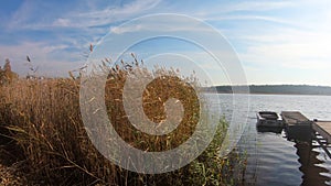 View on spikly grass, wooden pier, boat on blue river, calm and relaxation concept