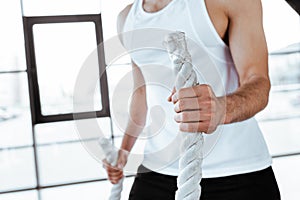 View of sportsman exercising with battle ropes in gym