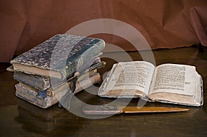 View at a stack of ancient stained books by an opened book and an old vintage knife