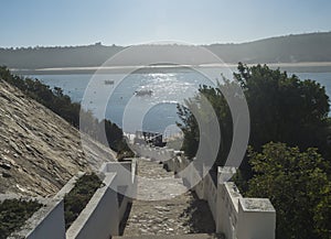 View of stairs leading to pier with small ferry boat across the river Mira flowing into the Atlantic Ocean. Vila Nova de