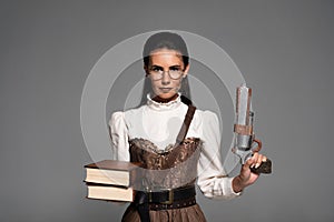 View of steampunk woman holding books and vintage pistol isolated on grey