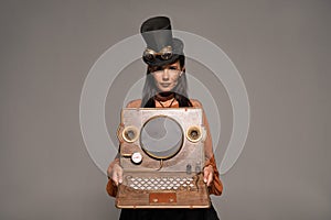 View of steampunk woman in top hat with goggles showing vintage laptop isolated on grey