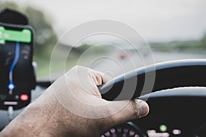 View of steering wheel, driverâ€™s hands, Google Maps on smartphone and the road,