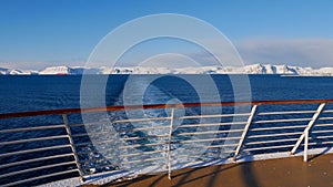 View from the stern of a cruise ship with the vessel\'s wake in the arctic ocean and snow-covered mountains near Hammerfest.