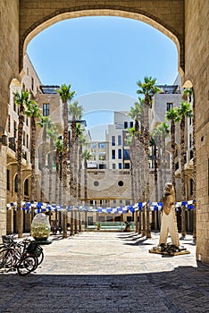 View through a stone gate on an empty square surrounded with palm trees and residential houses.