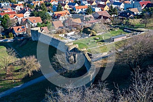 View of the stone wall of Devin Castle in Bratislava. There are autumn trees, lawn and houses in the surroundings