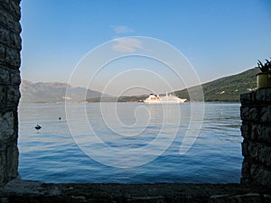 View from the stone wall of the sea Bay, where a white cruise ship is moving against the background of green mountains