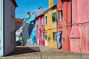 A view of street with colorful facades of houses and hanging laundry on a spring day with blue sky in famous island of Burano,