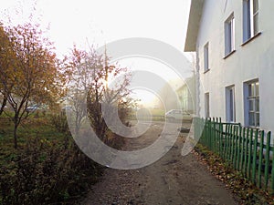 View on the street with path, fence, bushes and house in the morning.