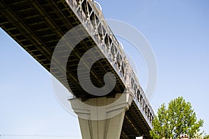 View of the structure of the highway bridge from below against the light blue sky. The road passes over the city, over the green