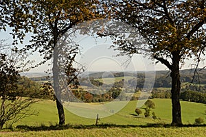 View in summer over the meadows with pasture fences and mountains of the Odenwald in Germany. The view is framed by two individual